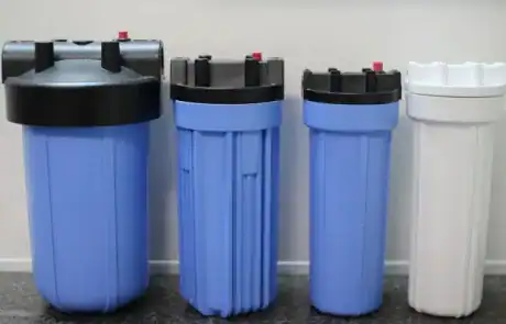 Four water filtration units, three blue and one white, on a gray countertop.