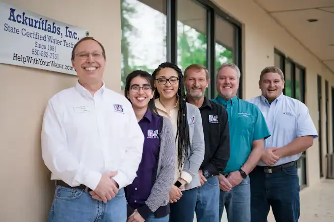 Group of five people standing outside Ackuritlabs, Inc. water testing business in a sunny setting.