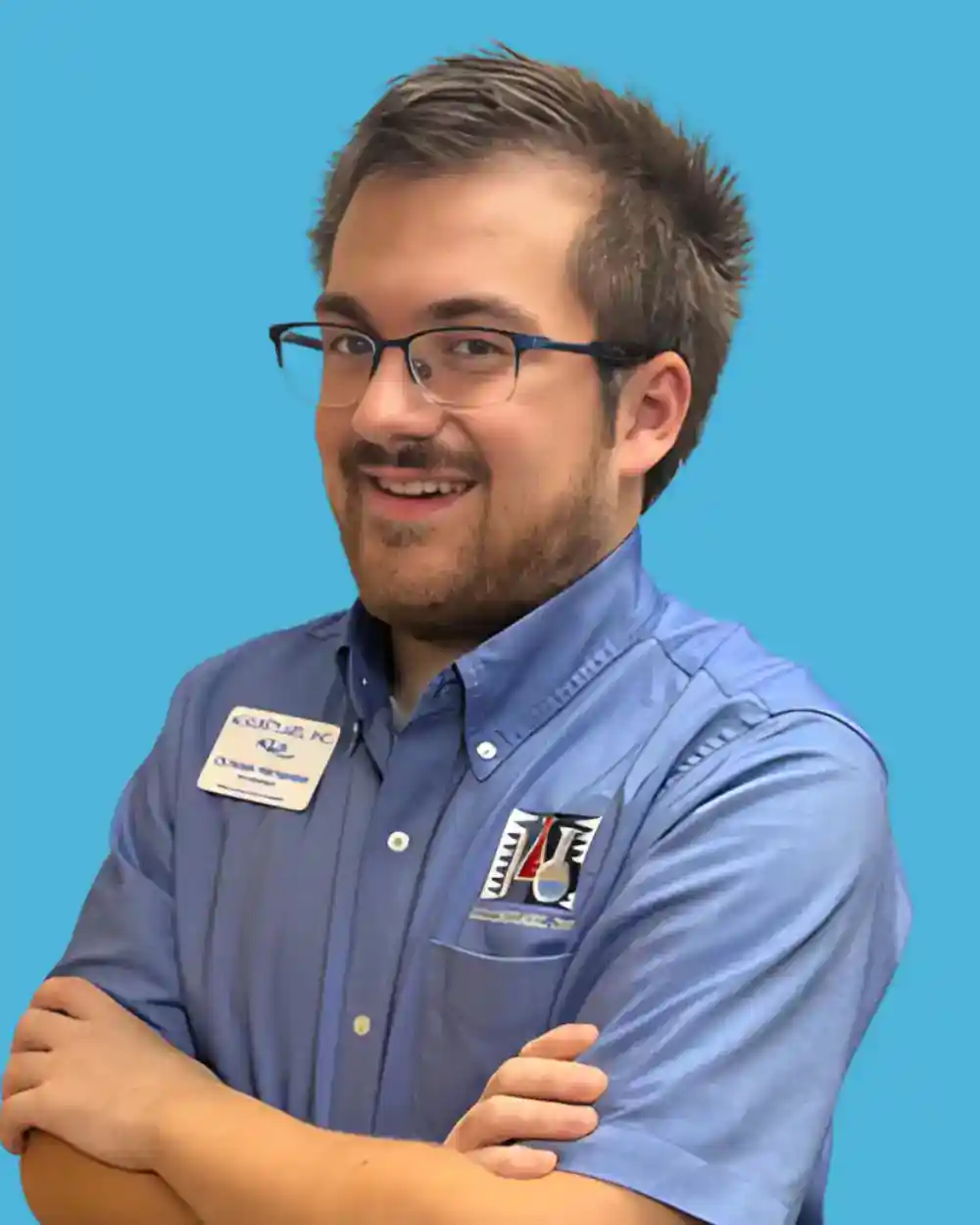 Young man in blue uniform with Ackuritlabs badge smiling against blue background.