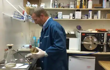 Technician in blue lab coat handling water sample in laboratory setting.