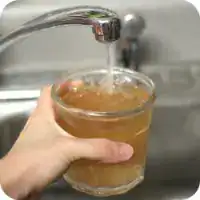 Person filling a glass with water from a kitchen faucet.