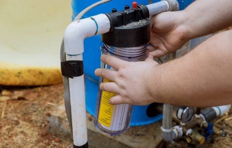 Technician installing a water filter on outdoor plumbing system in a residential setting.