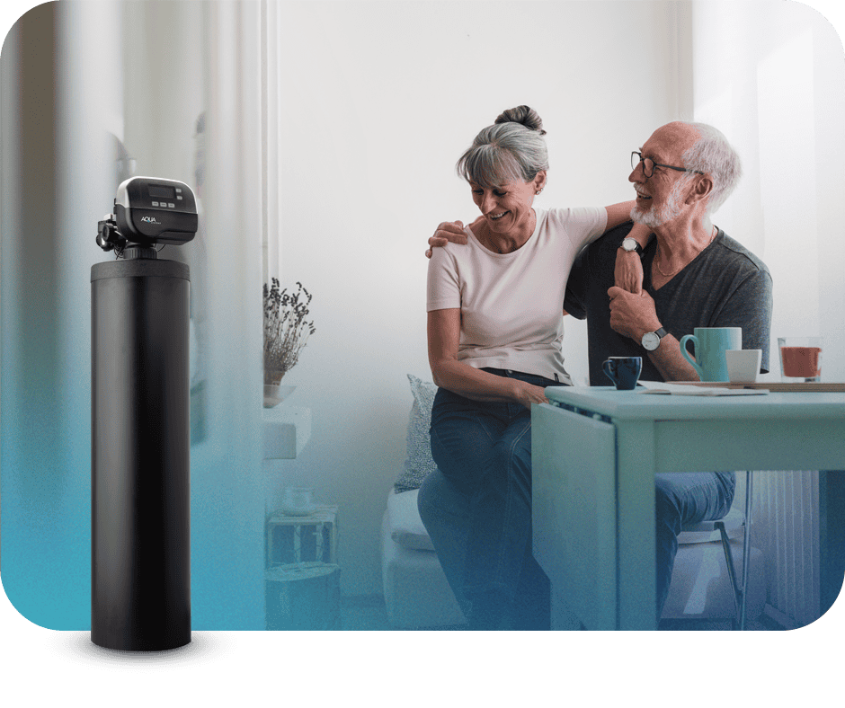 Elderly couple smiling at each other in a bright kitchen with a water testing device nearby.