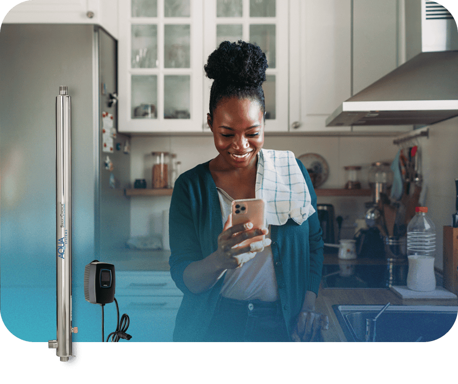 Woman smiling at her phone in a kitchen with water testing equipment nearby.