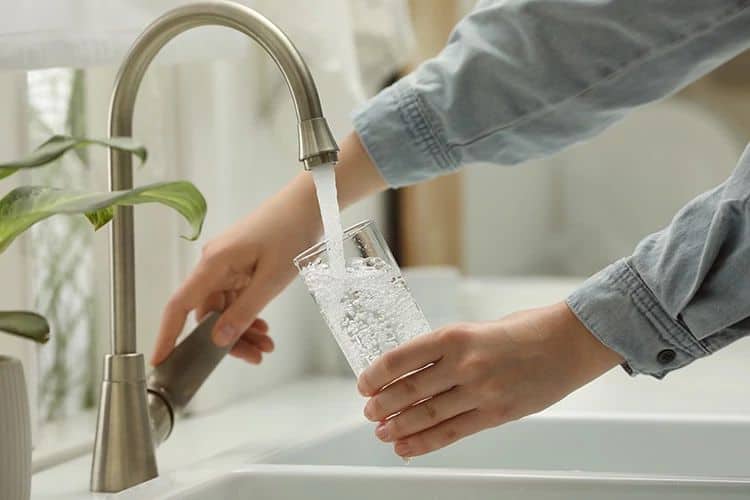 Person filling a glass with water from a kitchen faucet.