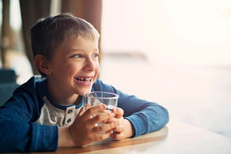 Child smiling and holding a glass of water indoors.