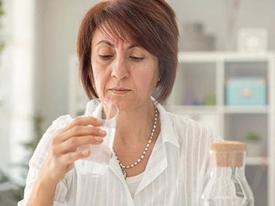 Woman tasting water sample in laboratory setting for water testing service.