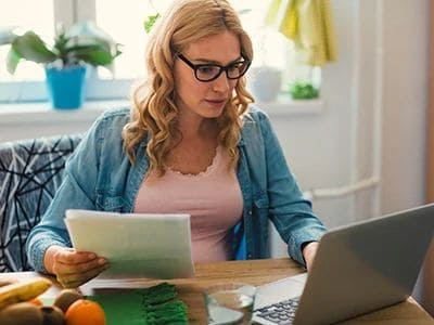 Woman working on a laptop with documents in a bright home office.