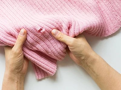 Person inspecting a pink knitted fabric for quality or damage.