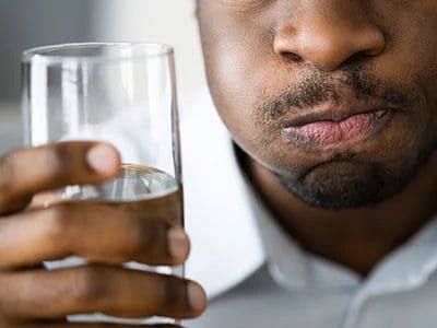 Close-up of a man holding a glass of water, focusing on his lips and the glass.