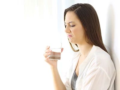 Woman inspecting a glass of water, concerned about water quality.