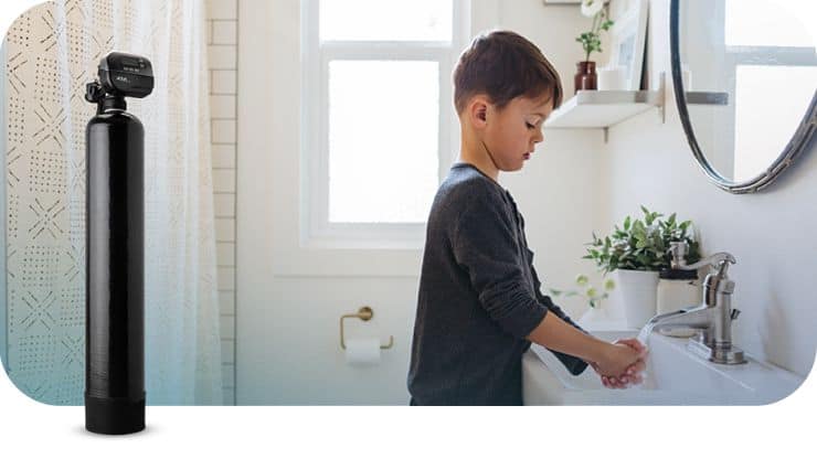Child washing hands at bathroom sink with water testing kit nearby.