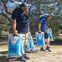 Two men carrying blue water testing kits outdoors in a park with trees.