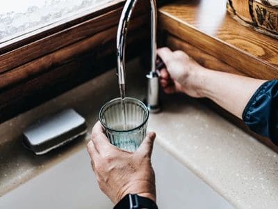 Person filling a glass with water from a kitchen sink tap.